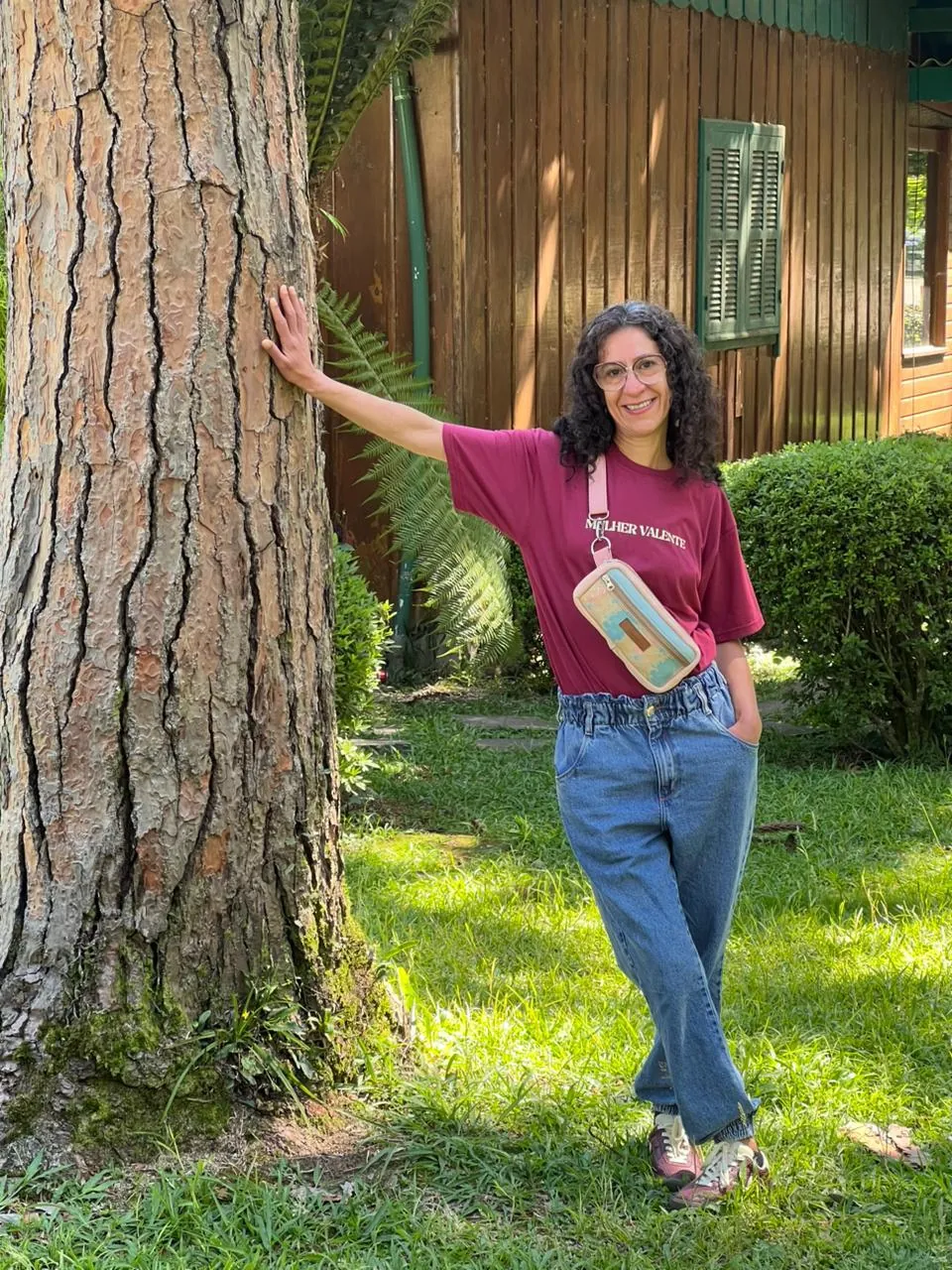 Mulher encostada numa árvore usando a Pochete Semente